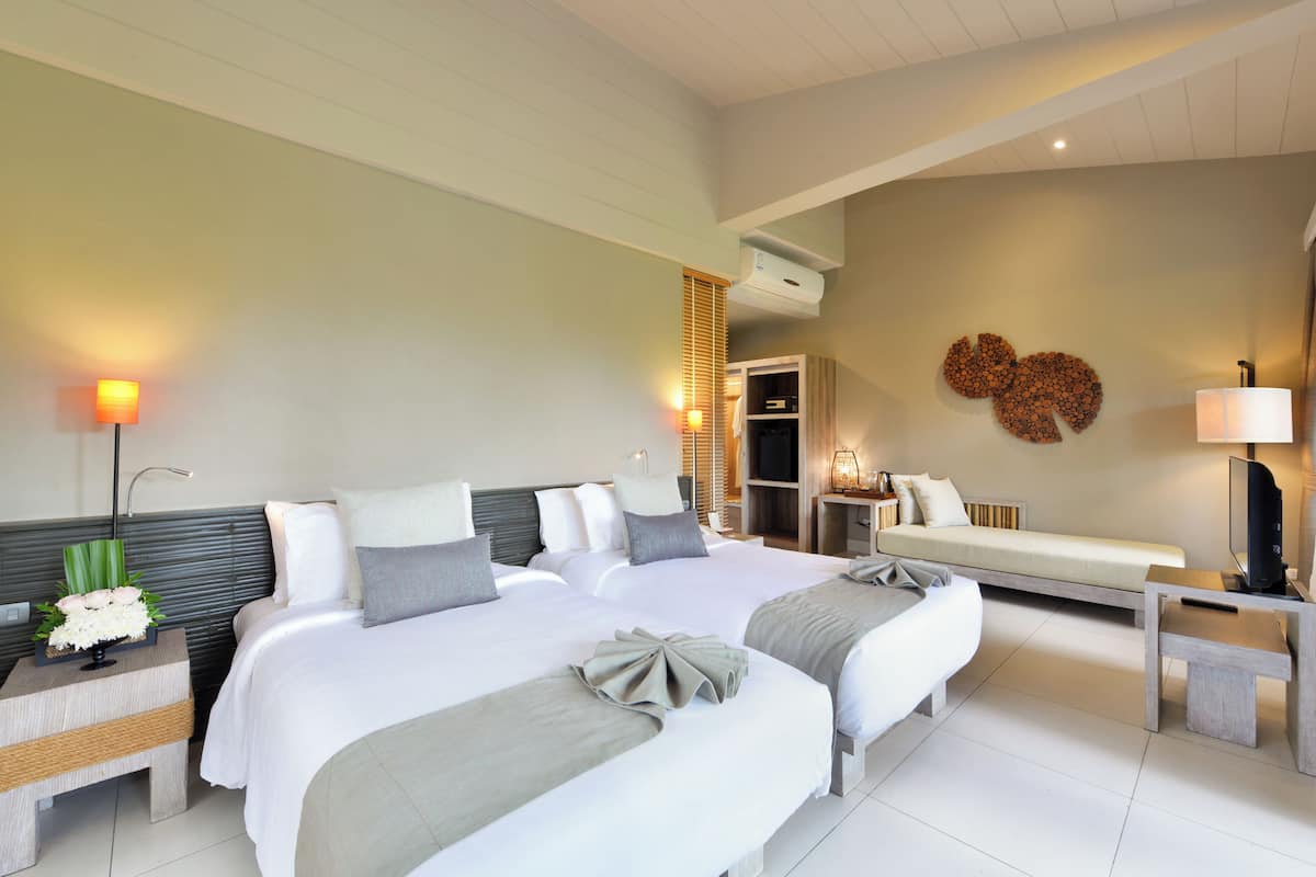 A hotel room with two beds, a desk, a TV, and a wall-mounted heater.
