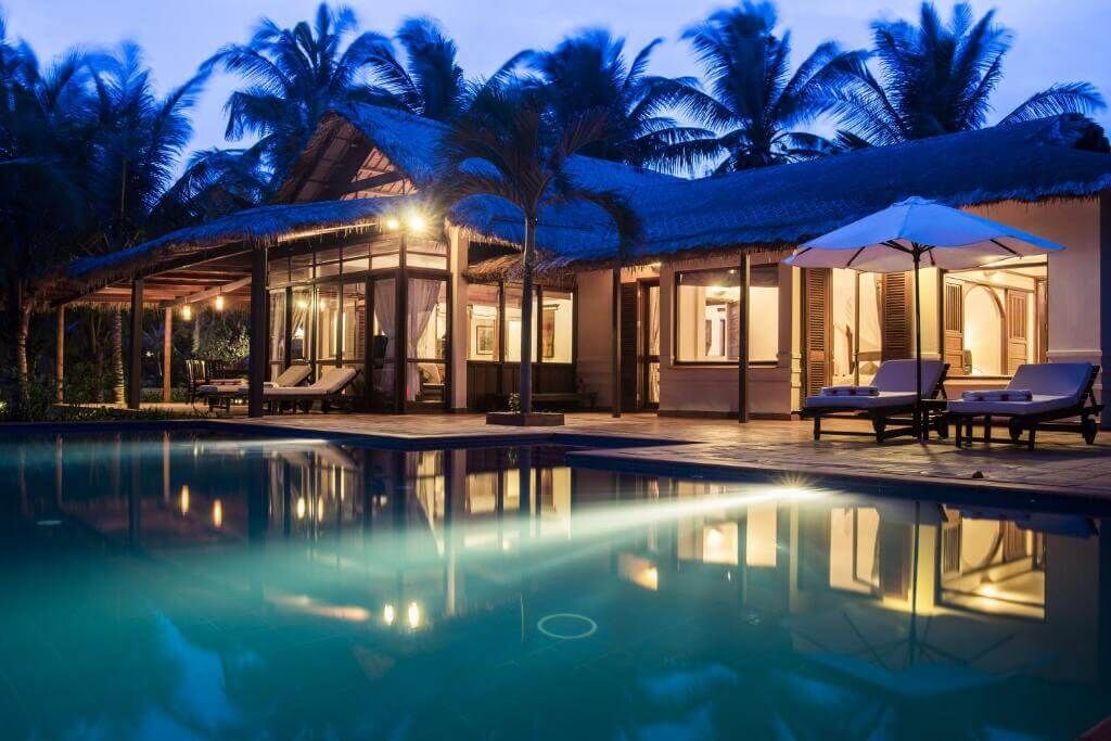 A poolside area with lounge chairs, a covered seating area, and a building with large windows.