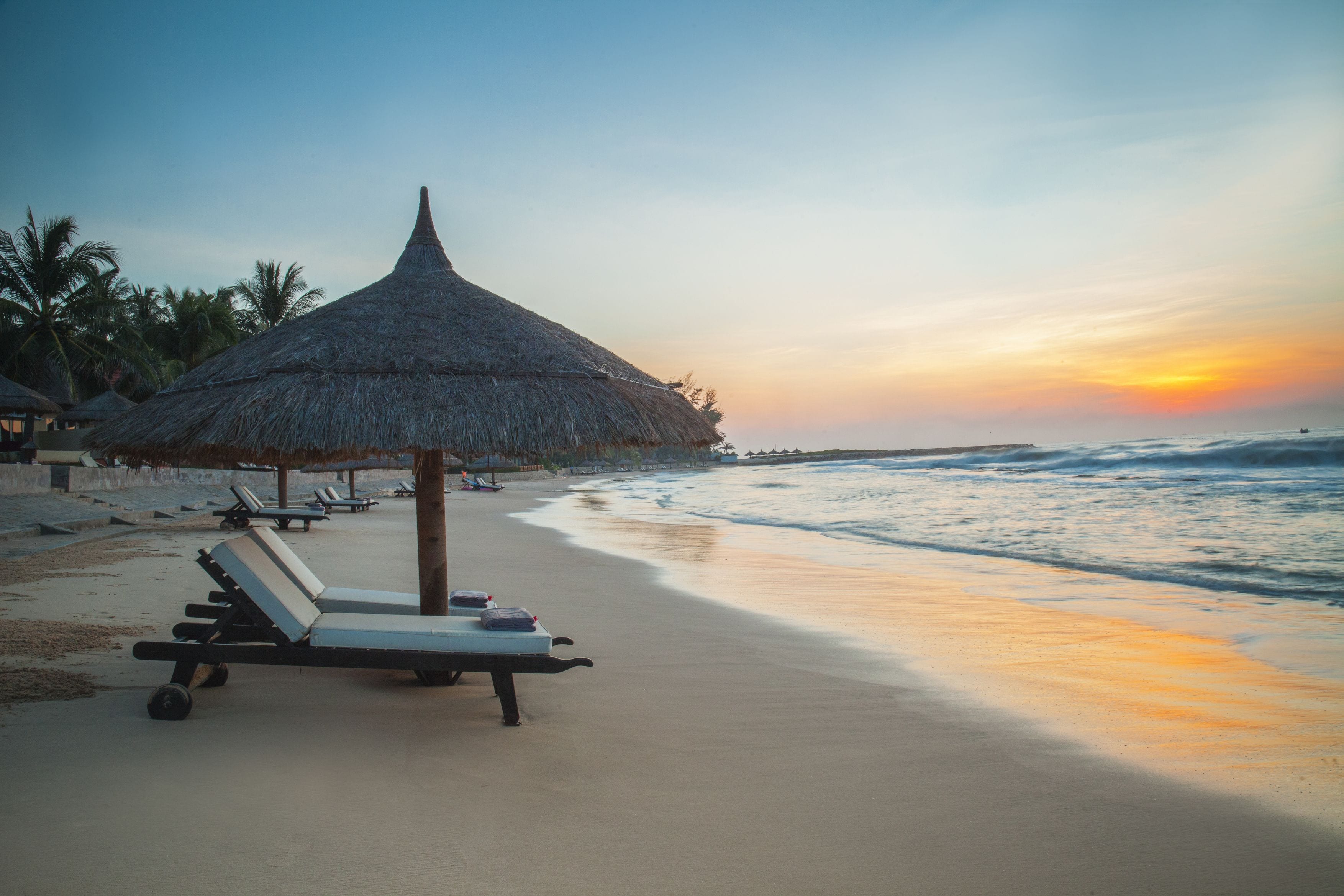 A beach with lounge chairs and a thatched umbrella, overlooking the ocean.
