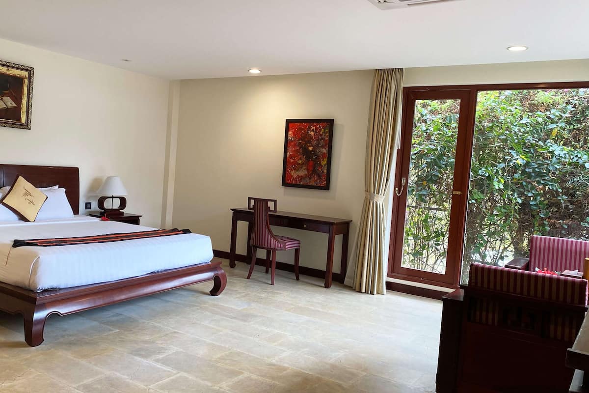 Une chambre d’hôtel avec un grand lit, un bureau, une chaise et une vue sur la verdure par la fenêtre.
