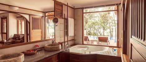 Un baño moderno con una bañera independiente, un espejo grande, muebles de madera y vistas al exterior.