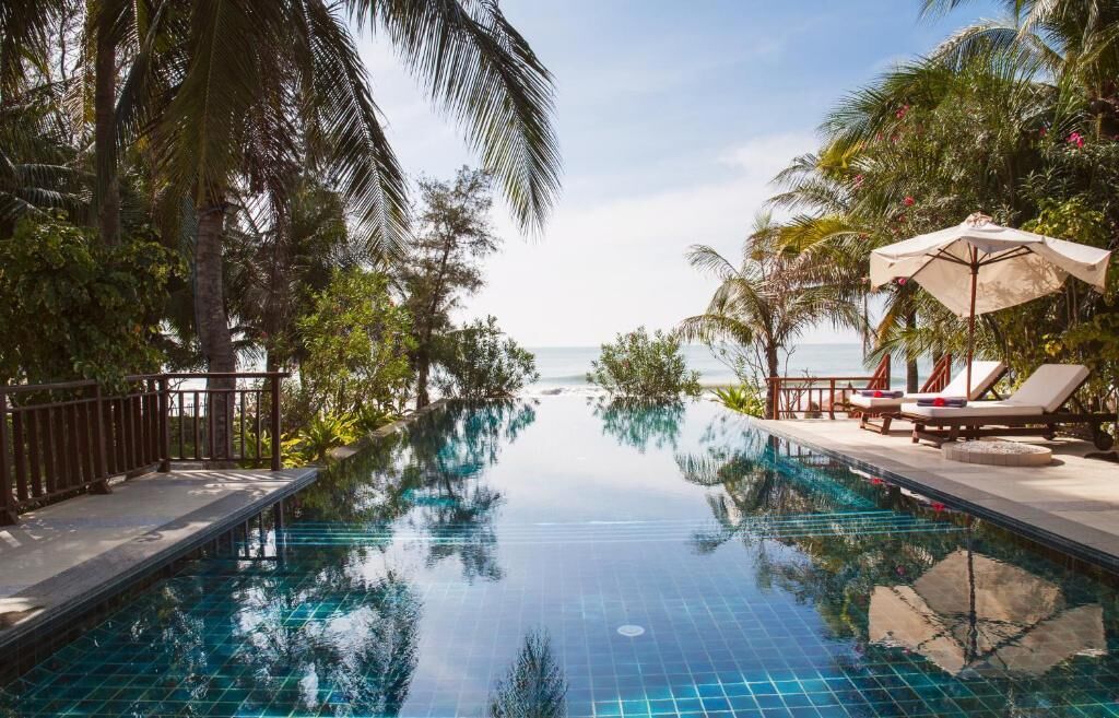 A pool with clear blue water, surrounded by palm trees and lounge chairs.