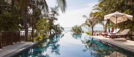 A pool with clear blue water, surrounded by palm trees and lounge chairs.
