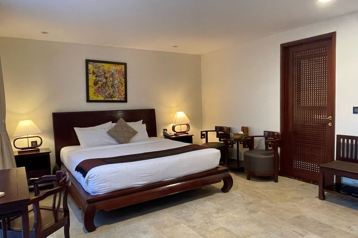 Une chambre d’hôtel avec un grand lit, deux tables de chevet avec des lampes, une porte en bois et une petite table avec des chaises.