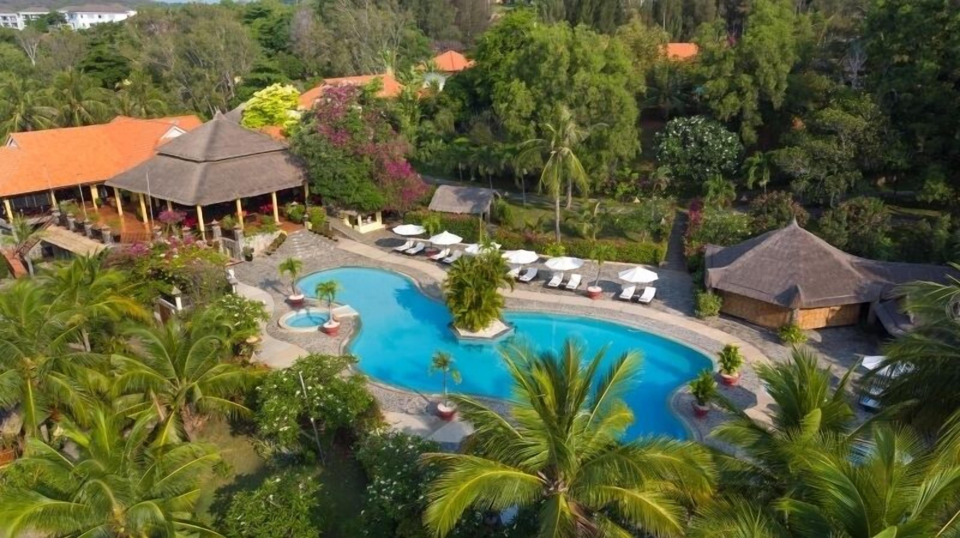 Een resort met een centraal gelegen zwembad, ligbedden en tropische beplanting.