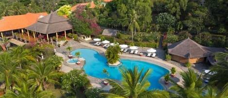 A resort with a central swimming pool, lounge chairs, and tropical vegetation.