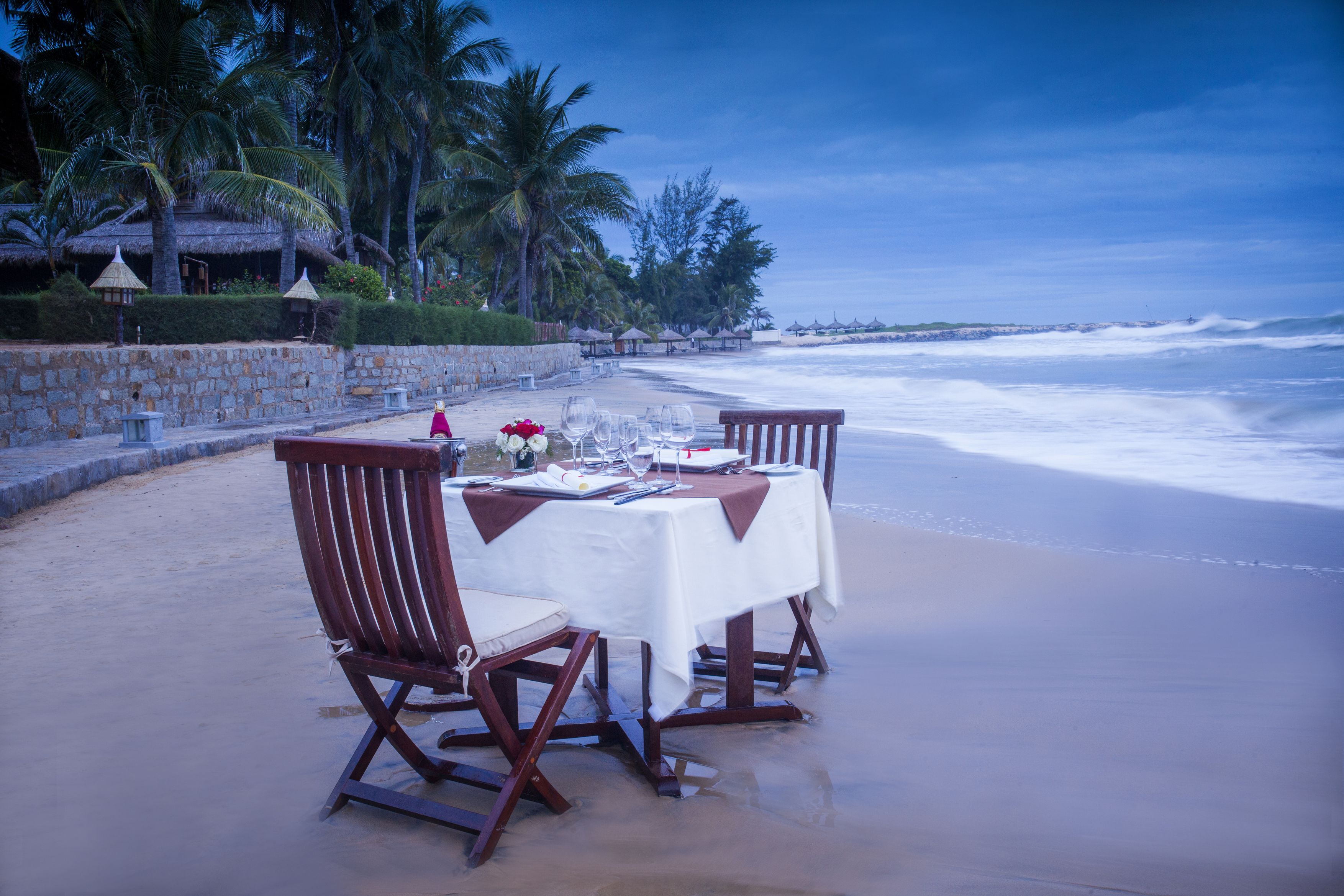 A beachfront dining setup with a table and chairs, overlooking the ocean.