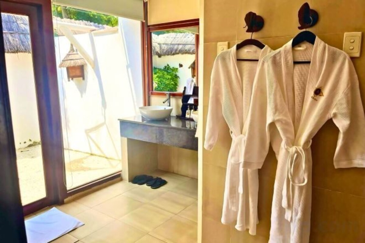 Une salle de bain avec un lavabo, un miroir et deux peignoirs blancs suspendus à un porte-serviettes.