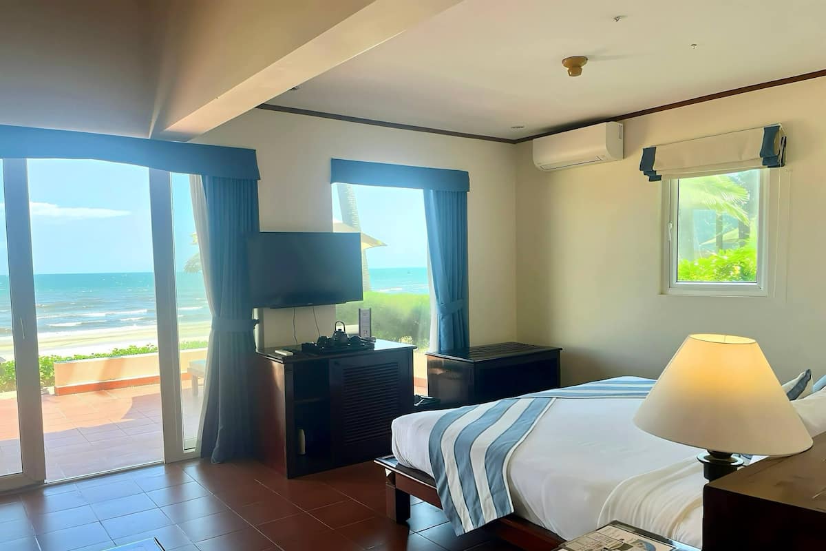 Une chambre d’hôtel équipée d’un lit, d’une télévision, d’un bureau avec une lampe, d’une fenêtre donnant sur l’océan et d’un appareil de climatisation.