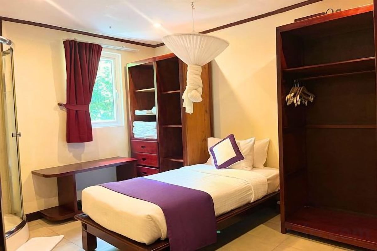 A bedroom with a bed, a wardrobe, a bedside table, and a window with curtains.