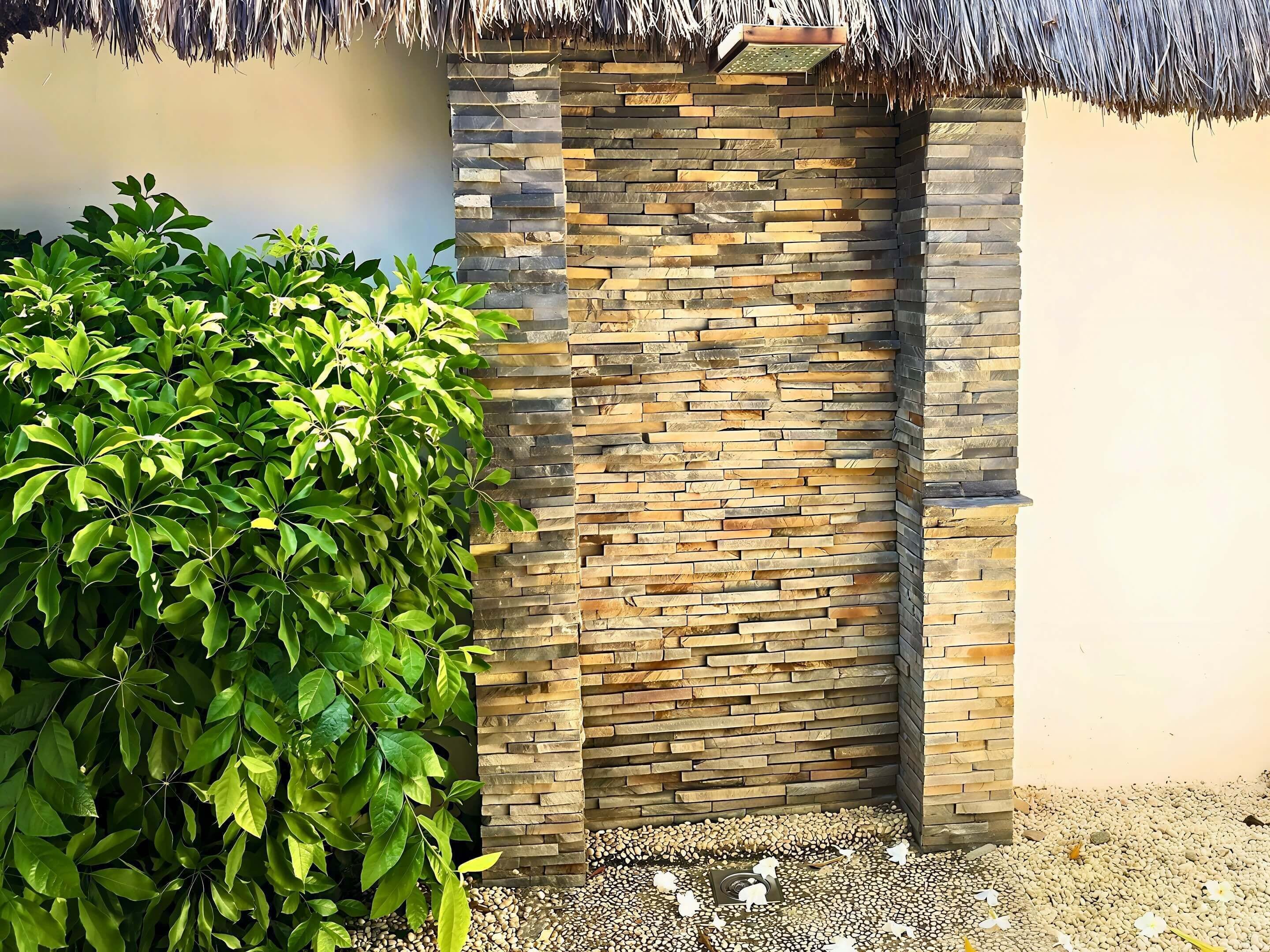 A stone wall with a thatched roof entrance, surrounded by lush green foliage.