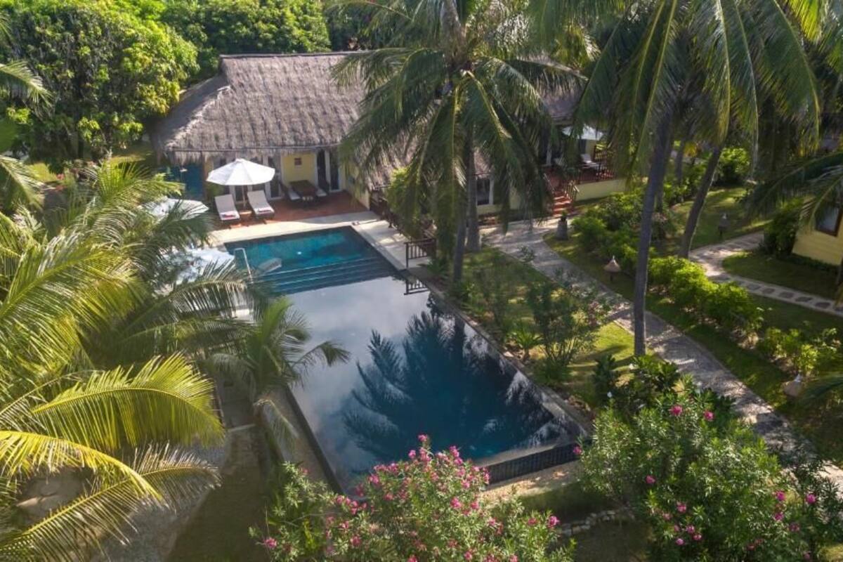 Un complexe hôtelier doté d’une piscine entourée de palmiers et d’un bâtiment à toit de chaume.