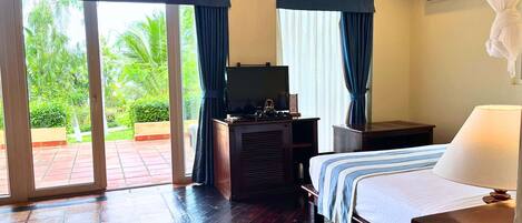 Habitación de hotel con cama, escritorio con televisor y vista a un jardín a través de una puerta corrediza.