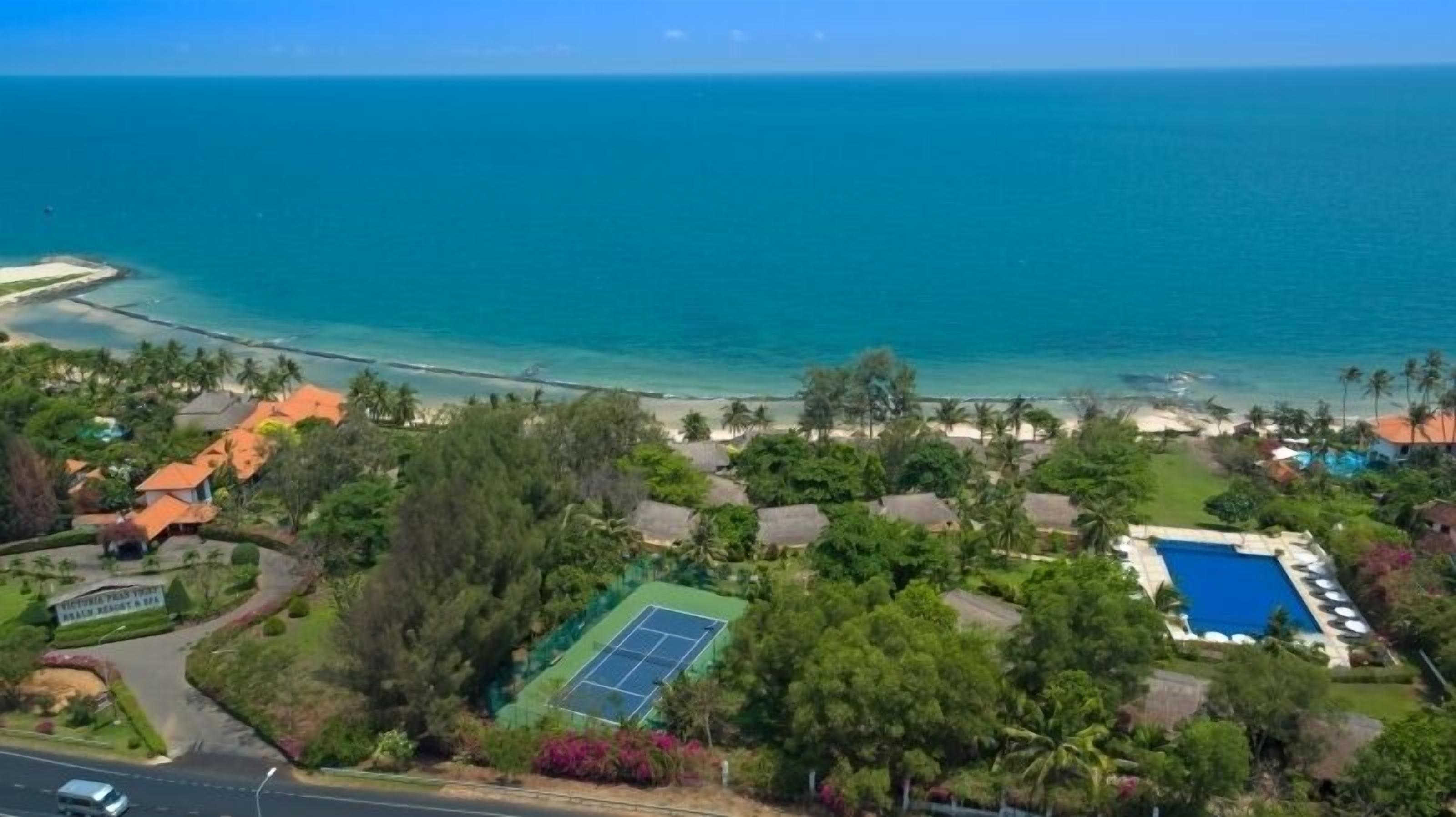 Un complejo turístico en la costa con cancha de tenis, piscina y acceso directo a la playa.