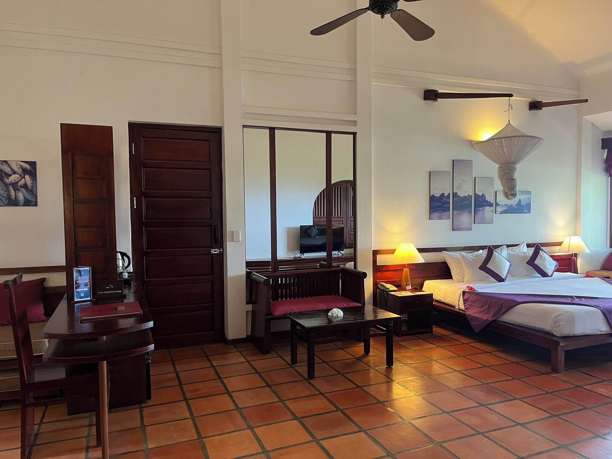 Una habitación de hotel con cama, escritorio, silla, televisor y ventilador de techo.