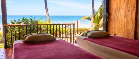 A room with two beds, a wooden ceiling, and a view of the ocean.