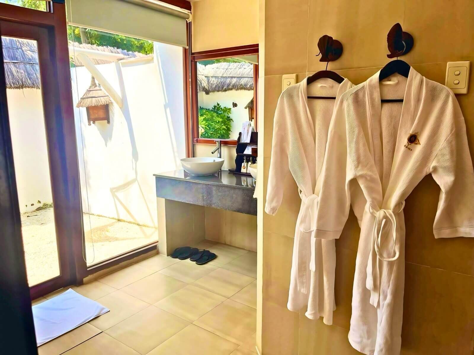 A bathroom with a sink, mirror, and two white robes hanging on the wall.