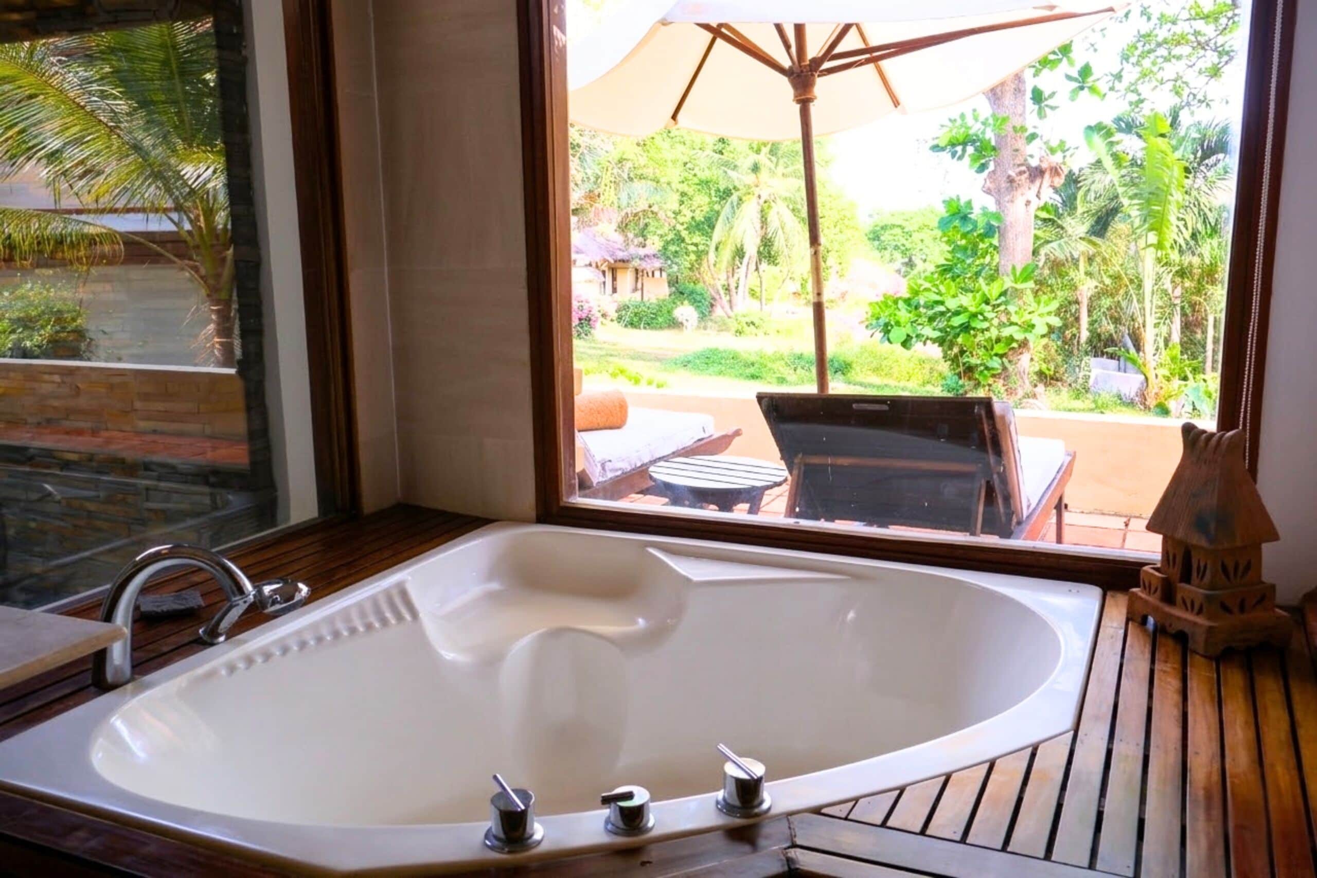 A large bathtub with a window view of a garden and outdoor furniture.