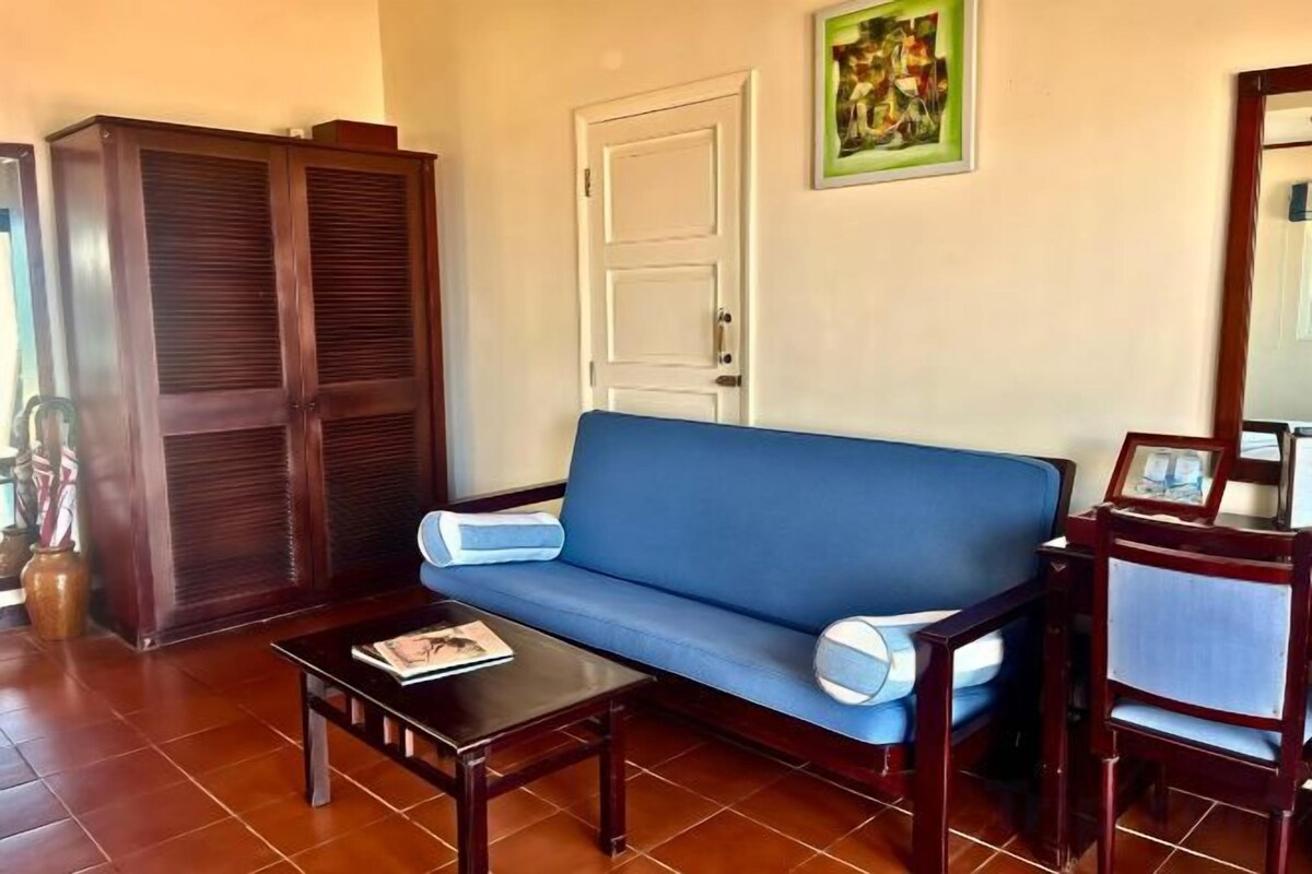 Un salon avec un canapé bleu, une table basse en bois, une chaise en bois et une armoire.