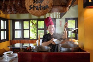 Un chef en una cocina con un wok grande, un menú colgante y una ventana con vistas a zonas verdes.