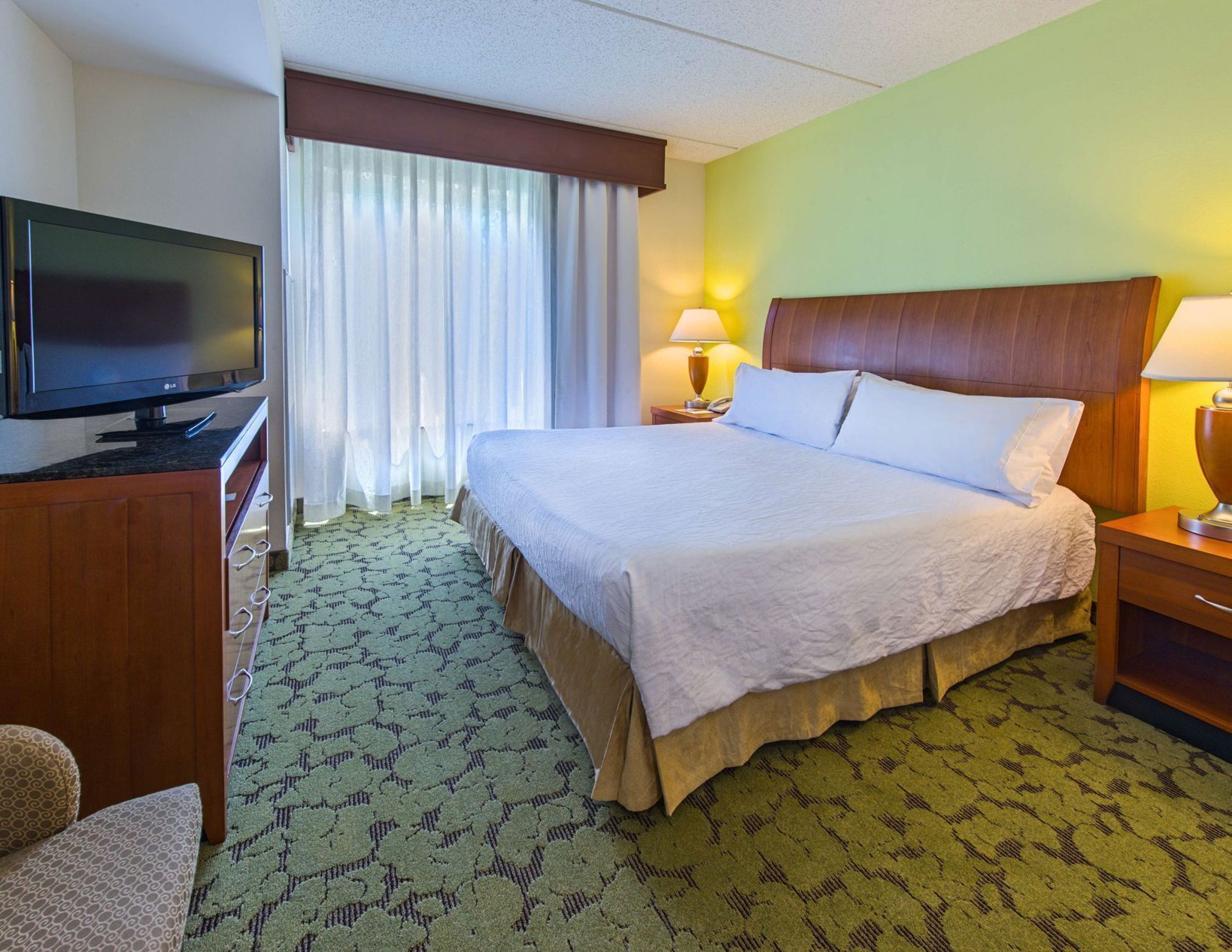 A hotel room with a bed, a TV, a desk, and a lamp.