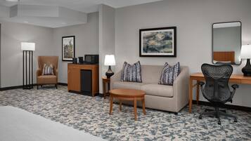 A hotel room with a sofa, armchair, desk, and a small table.