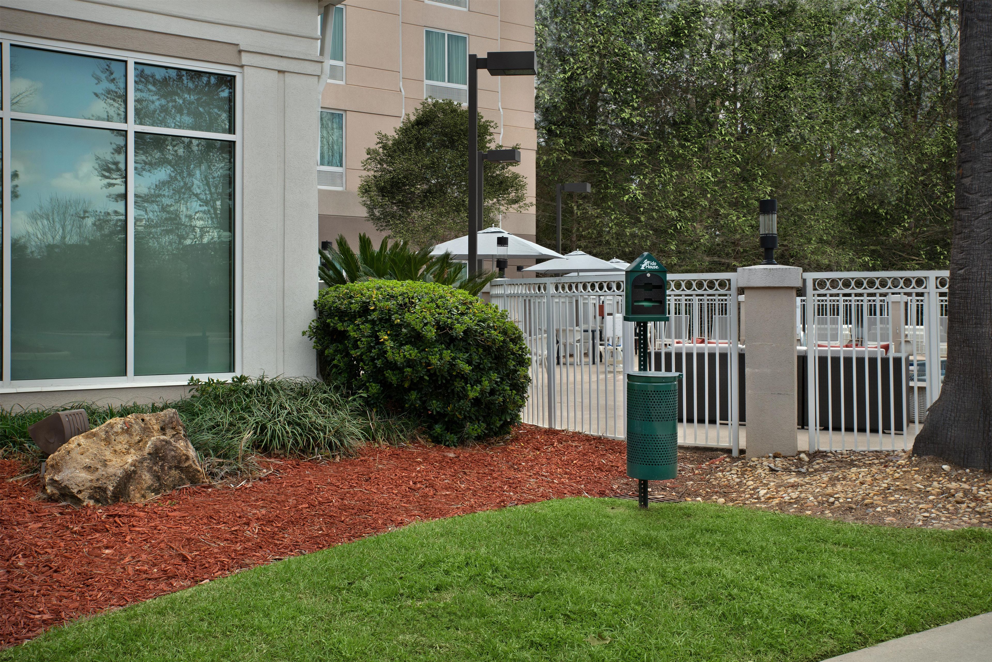 A gated entrance with a mailbox, a small hedge, and a building with large windows.