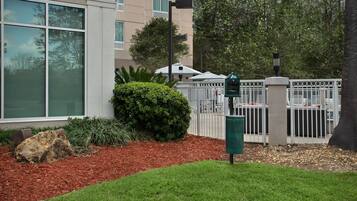A gated entrance with a mailbox, a small hedge, and a building with large windows.