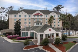 A multi-story hotel with a central entrance, a swimming pool, and landscaped gardens.