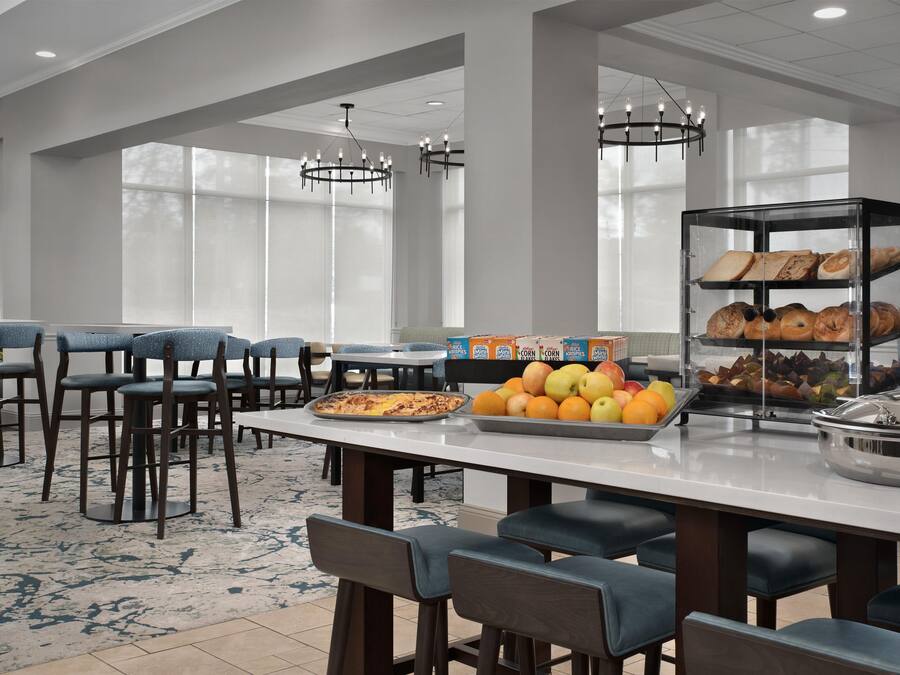 Espaço de refeições de hotel com buffet, mesas e uma grande janela.