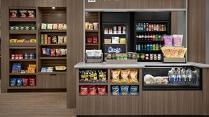 Mostrador de aperitivos y bebidas en una tienda con estantes llenos de varias marcas y productos.