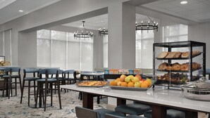 Comedor de hotel con mesas, sillas, un bufé de frutas y pasteles, y una araña.