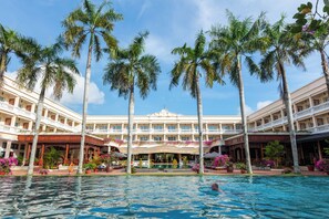 A hotel with a swimming pool surrounded by palm trees and potted plants.