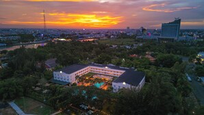 A large hotel with multiple floors and a swimming pool, surrounded by greenery and a cityscape in the background. - Victoria Can Tho Resort (Can Tho)