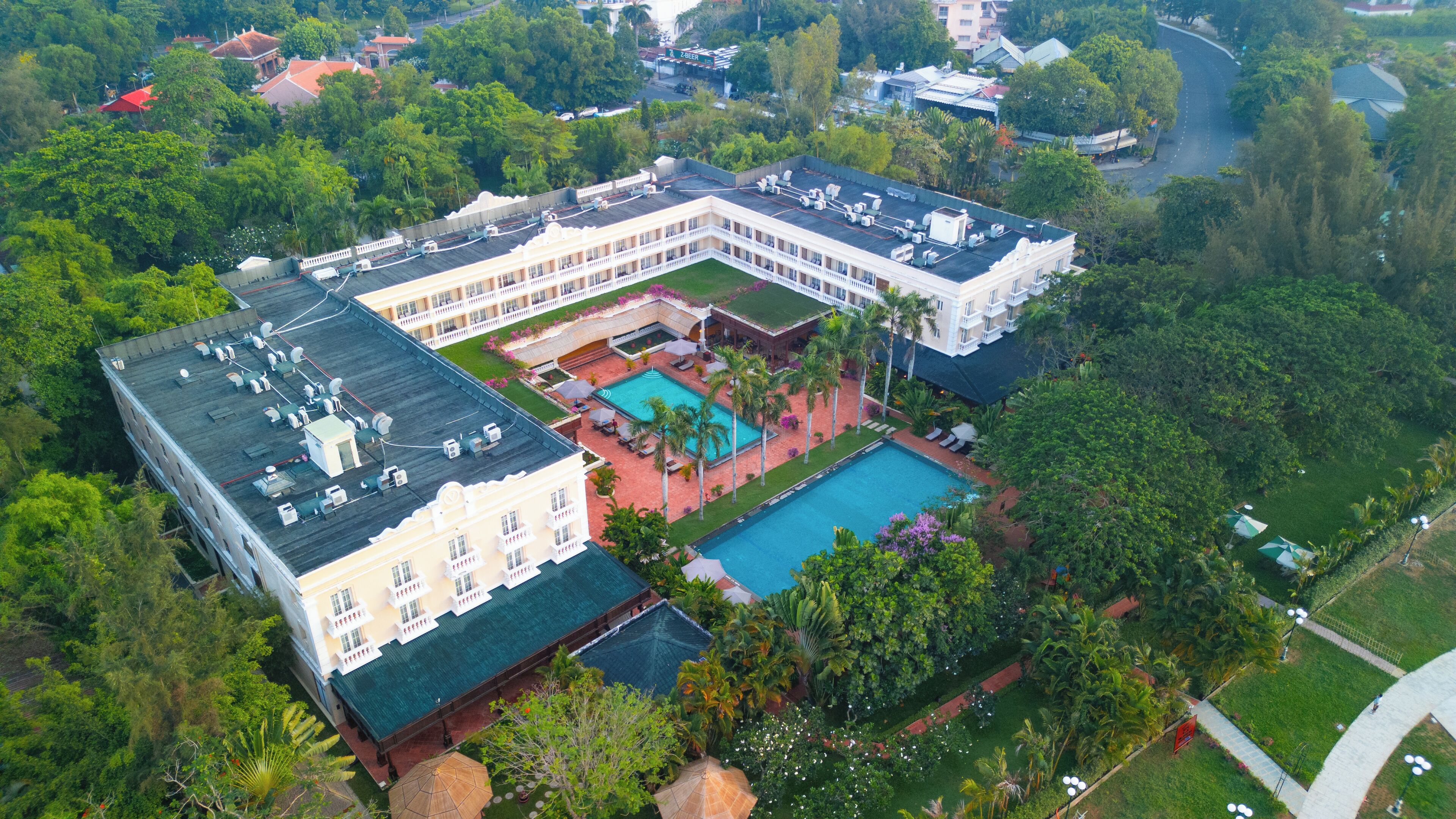 Un gran hotel con varias secciones, un patio central con piscina y abundante vegetación circundante.