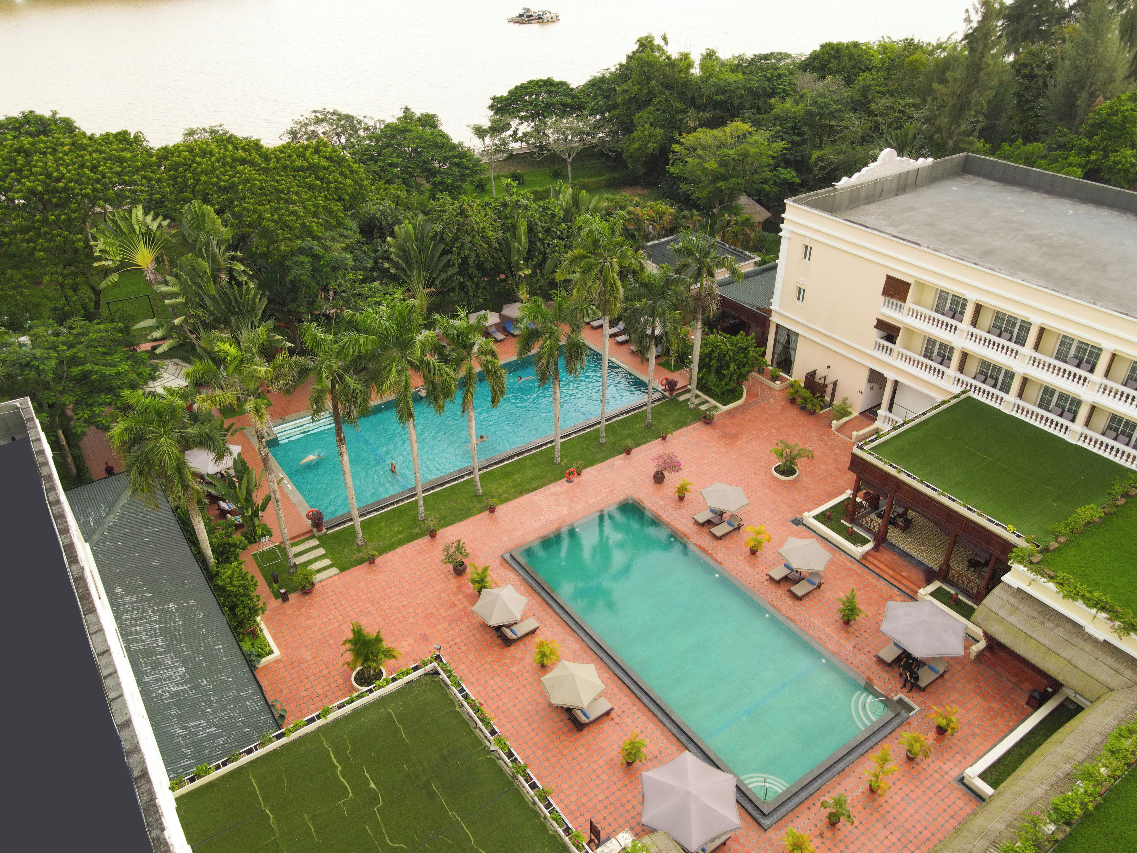 Un área de piscina en la azotea con dos piscinas, rodeada de palmeras y un edificio con balcones.