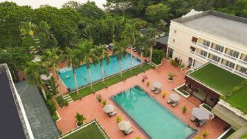Un área de piscina en la azotea con dos piscinas, rodeada de palmeras y un edificio con balcones.