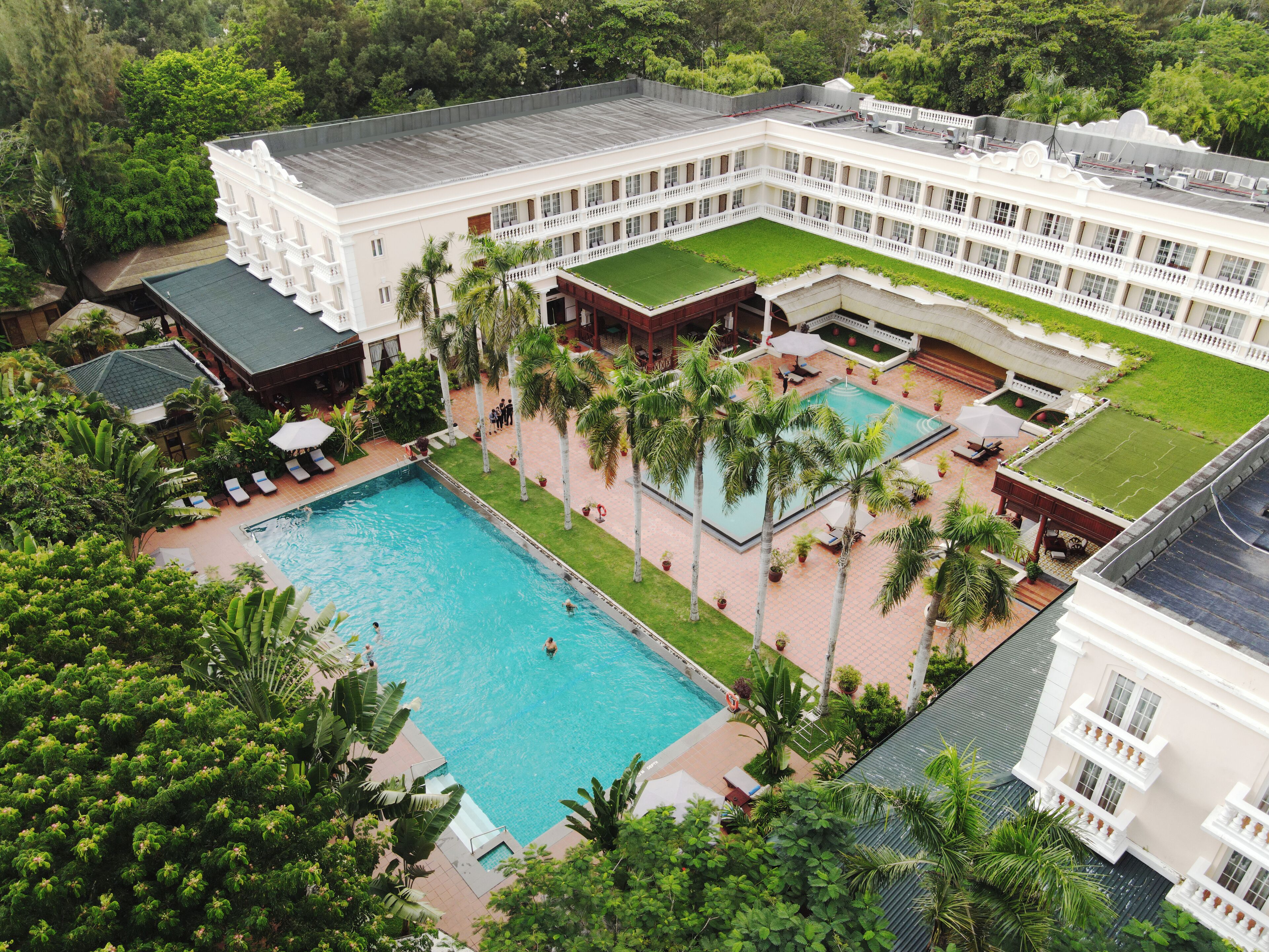 A large hotel with a swimming pool surrounded by palm trees and a well-maintained lawn.