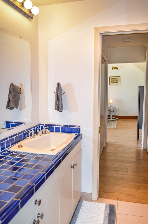A bathroom with a blue-tiled sink, white cabinets, and a mirror.