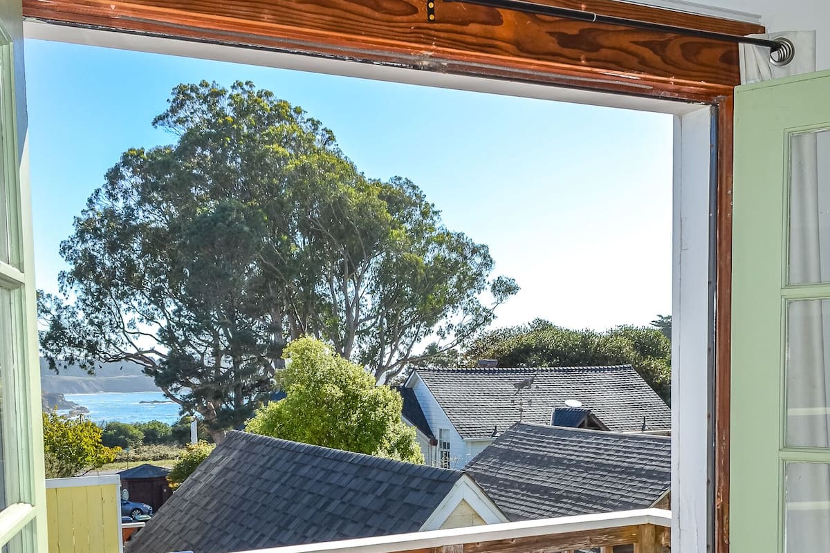 Eine Holzterrasse mit einem roten und gelben Stuhl, einem kleinen Tisch und Blick auf Häuser und Bäume.