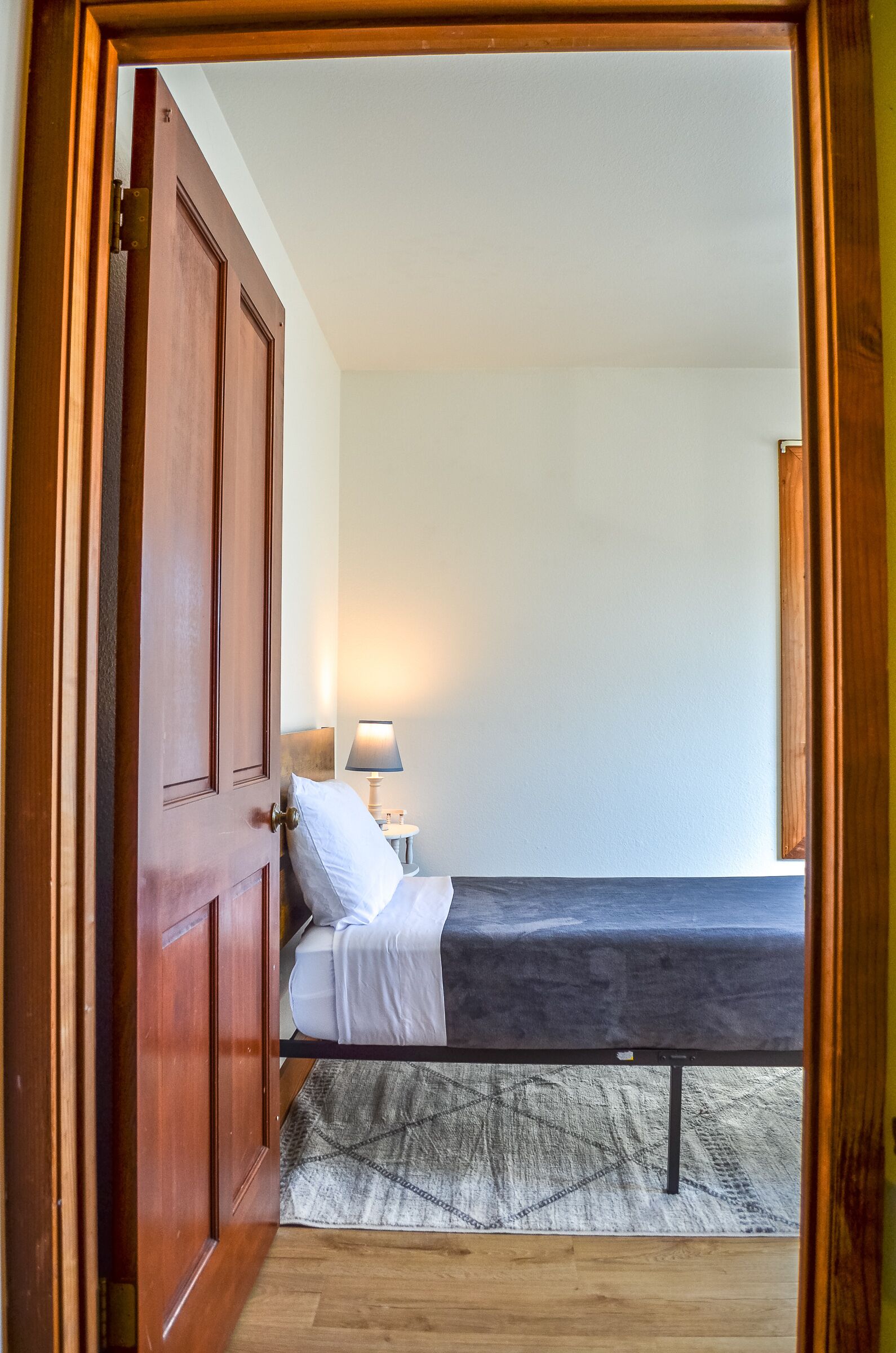 A room with a bed, a nightstand with a lamp, and a wooden door.