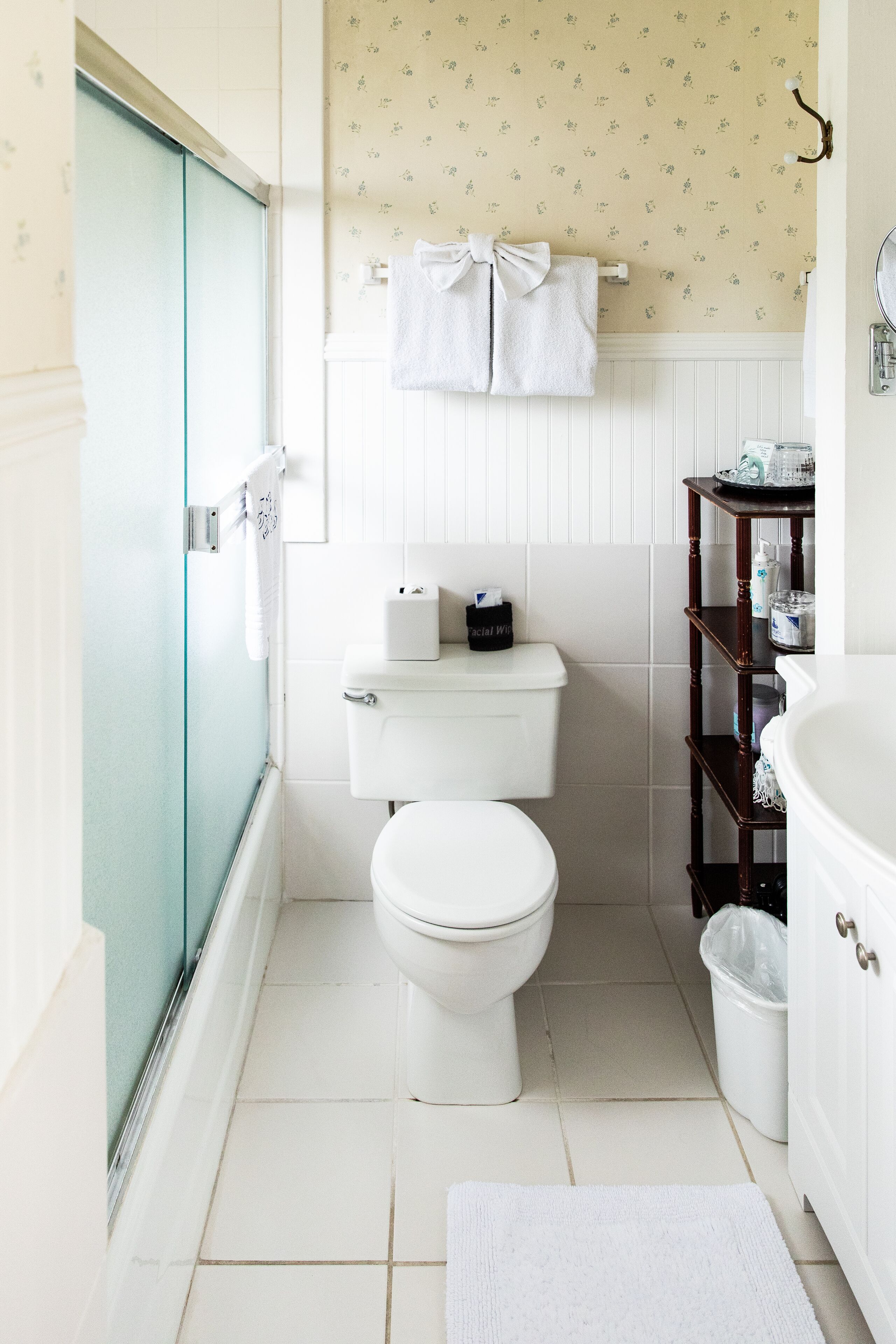 A bathroom with a toilet, a glass shower enclosure, a white sink, and a vanity with shelves.
