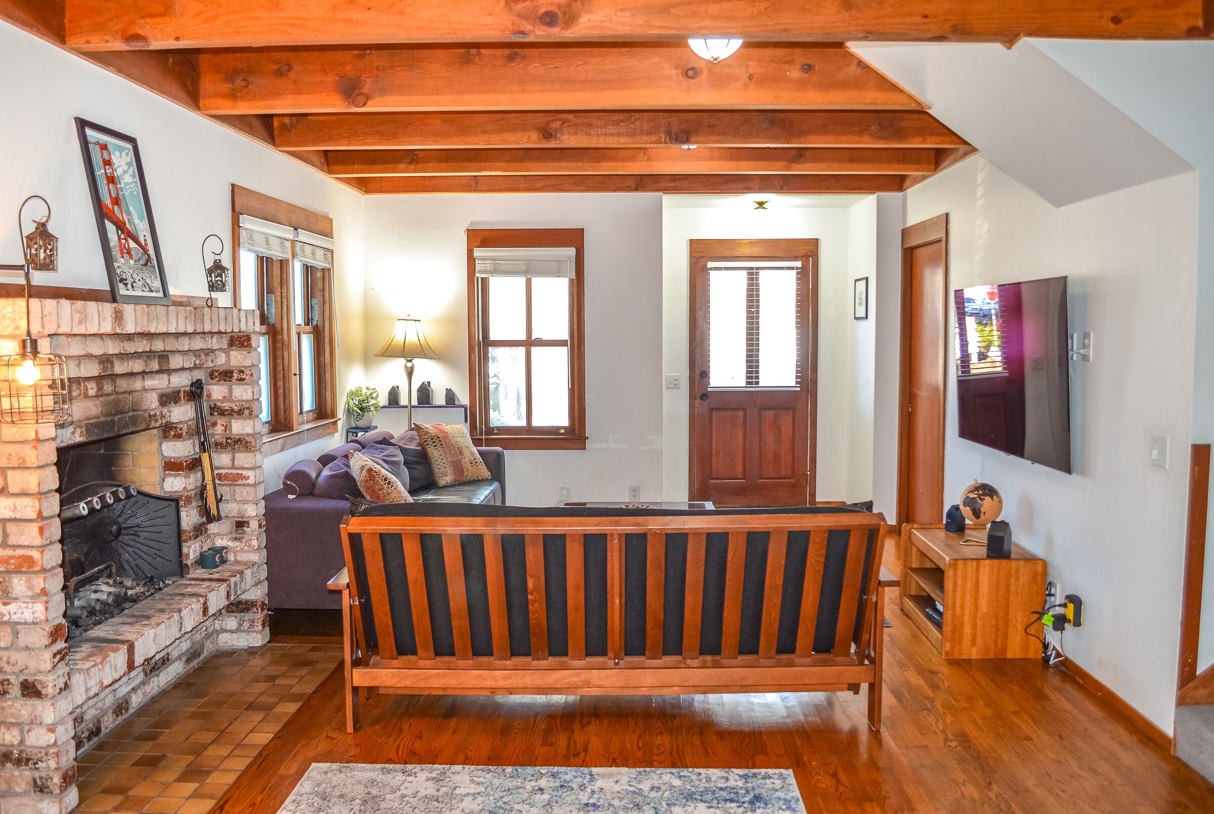 Un salón acogedor con chimenea de ladrillo, vigas de madera, un sofá y una televisión.