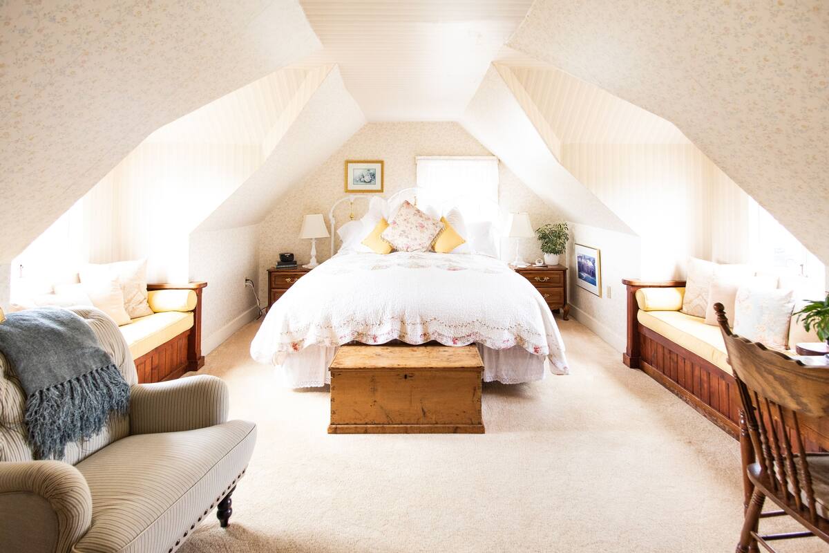 Ein gemütliches Schlafzimmer im Dachgeschoss mit einem großen Bett, einer hölzernen Bank und einem Stuhl.