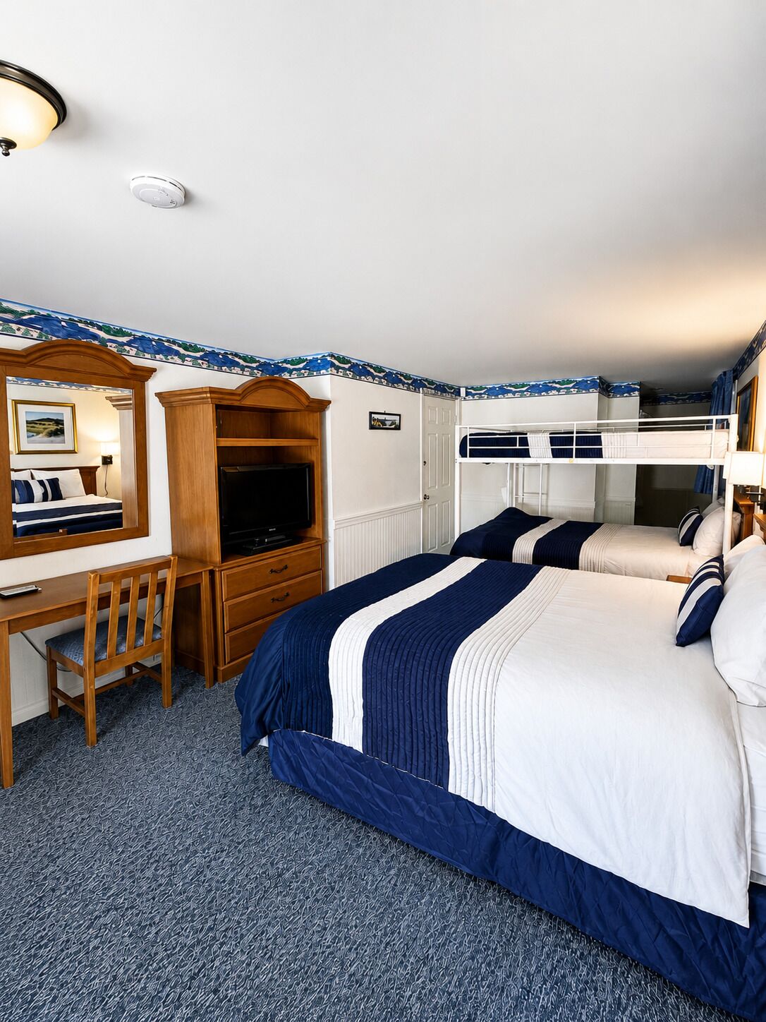 A hotel room with a bunk bed, a desk with a chair, a television, and a wardrobe.