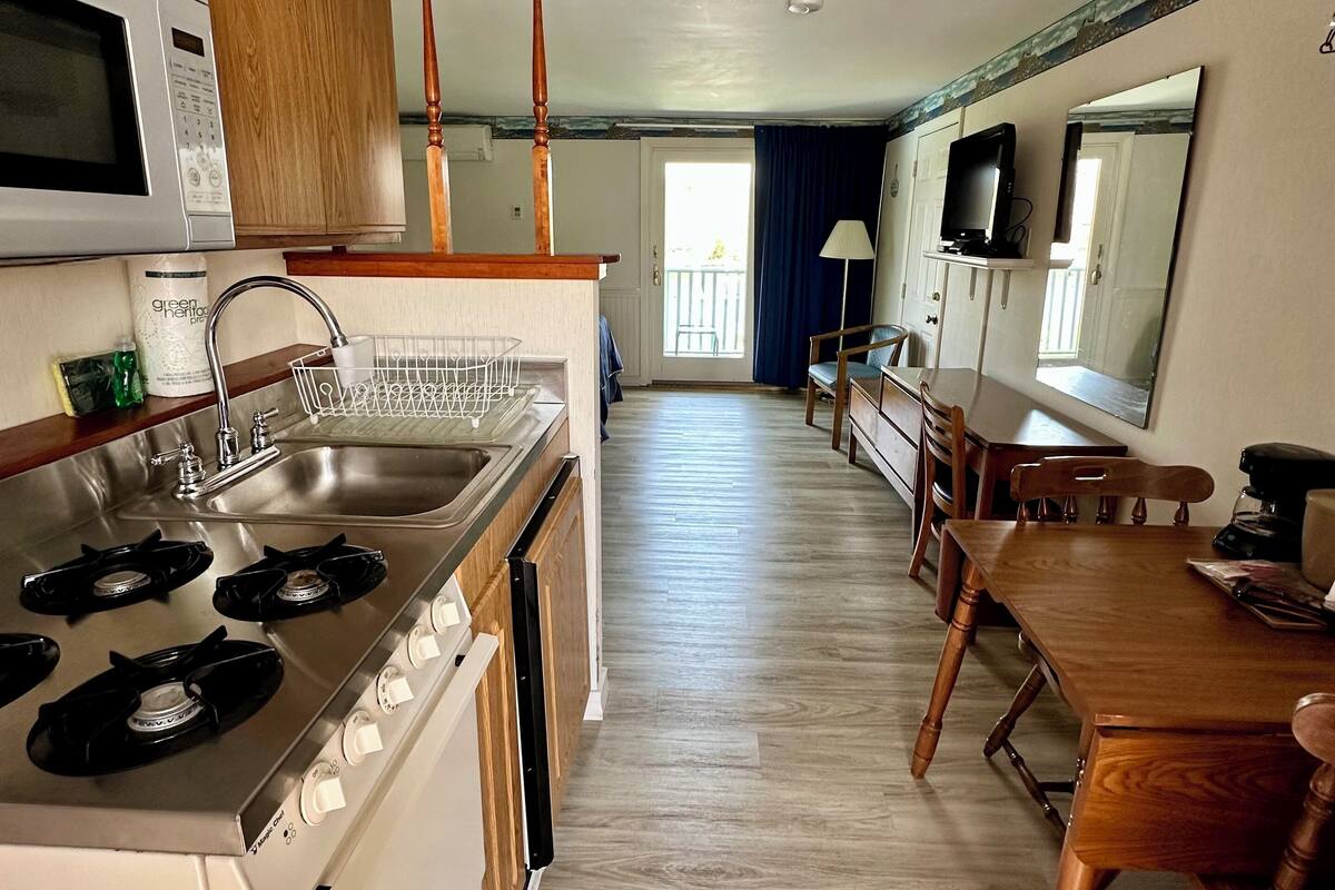 A kitchen with a stove, sink, and microwave. There is a dining table with chairs and a TV mounted on the wall.