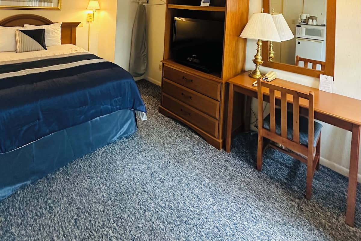 A hotel room with a bed, a TV, a desk with a lamp, and a mirror.