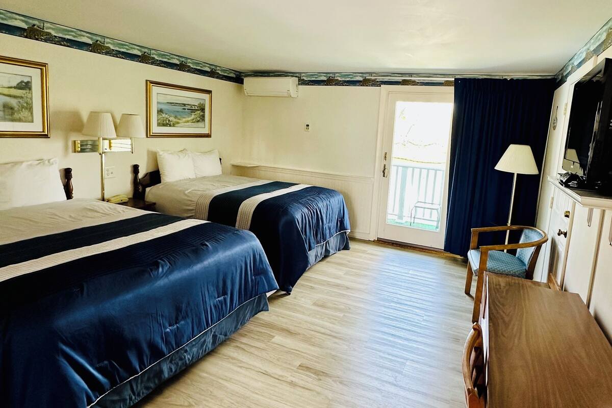 A hotel room with two beds, a wooden desk, a chair, a TV, and a window with a view.