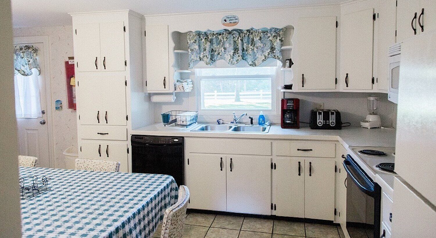 Una cocina compacta con armarios blancos, un fregadero, una estufa y un lavavajillas.