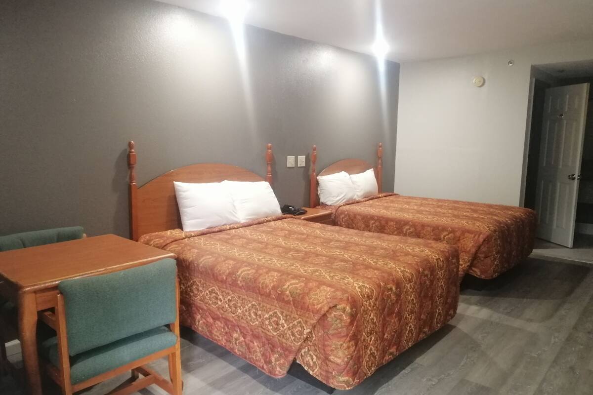 A hotel room with two beds, a wooden nightstand, a desk, and a chair.